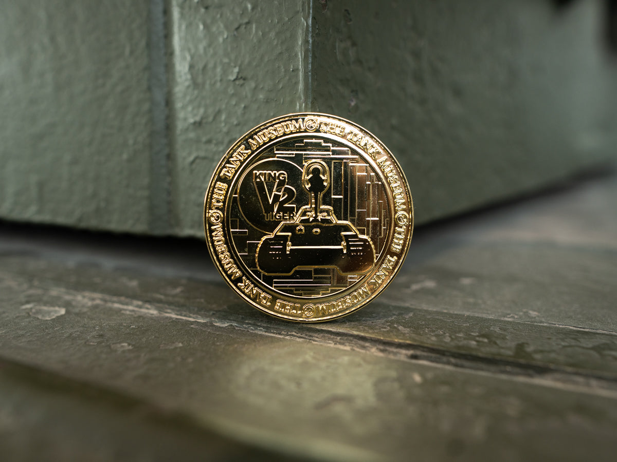 A gold-colored commemorative medallion, showcasing a design of the King Tiger V2 tank with The Tank Museum logo on the edges