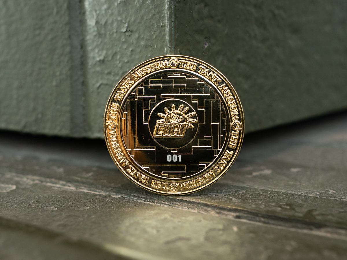 A gold-colored commemorative medallion featuring the COBI logo in the middle with an individual number on the back (001) with The Tank Museum logo on the edges. 