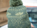 A man modelling a two-tone green knitted design bobble hat, with The Tank Museum logo on the cuff. Finished with a debossed faux-leather Tank Museum tab.