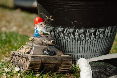 Gnome on a tank toy next to a potted plant in a garden setting
